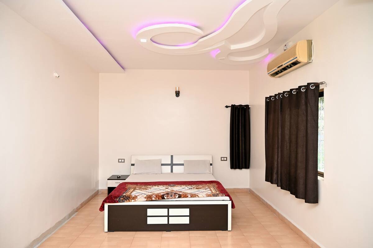 Un dormitorio con cama, mesita de noche, aire acondicionado instalado en la pared y ventana con cortinas.