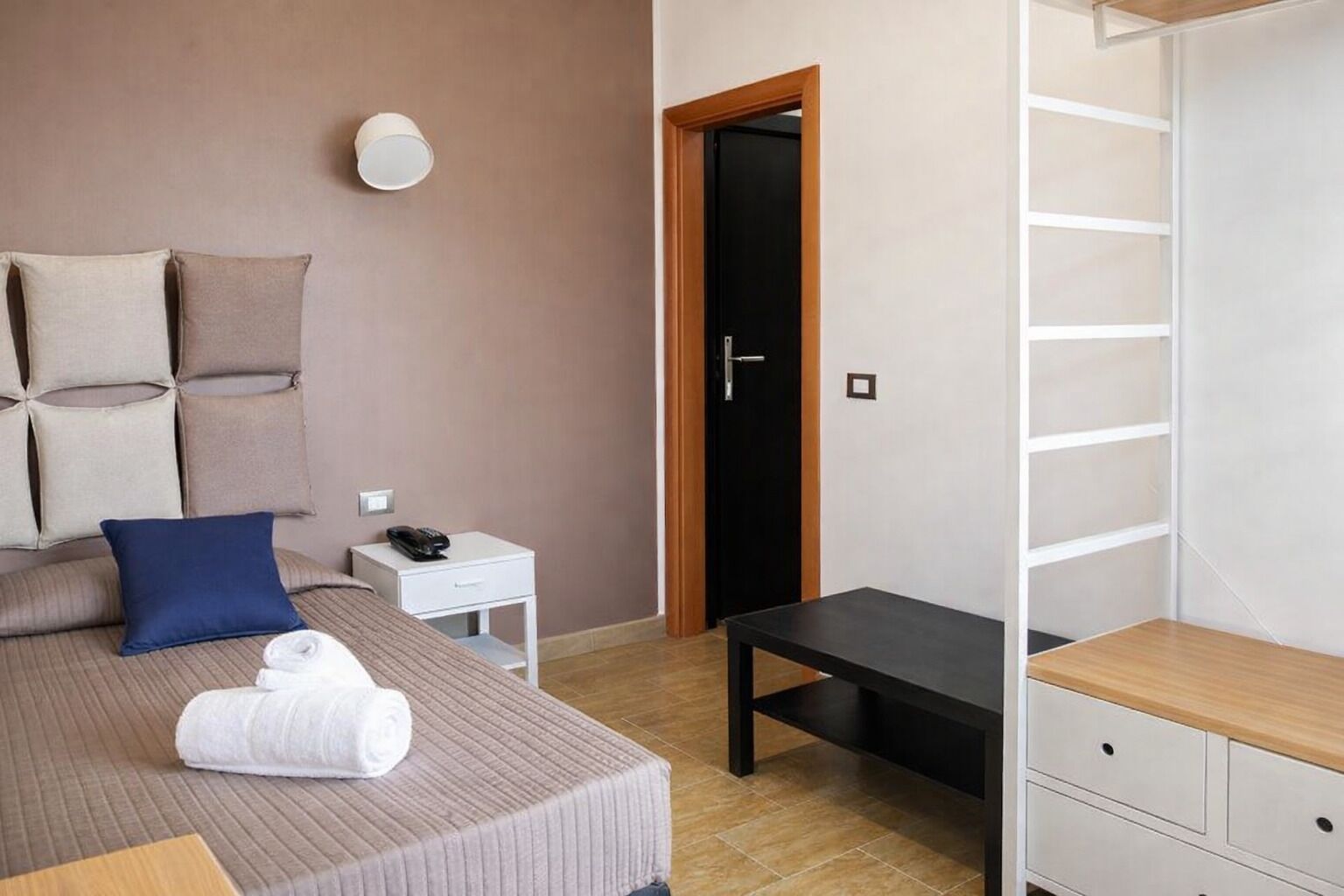 A hotel room with a bed, bedside table, a desk, a chair, a wardrobe, and a door.