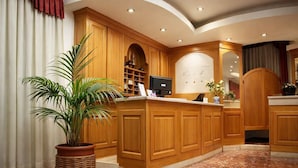 Zona de recepción con muebles de madera, una planta en maceta, mostrador de recepción y un monitor.