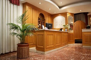 Zona de recepción con muebles de madera, una planta en maceta, mostrador de recepción y un monitor.