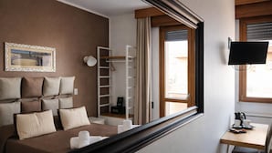 Habitación de hotel con cama, escritorio, televisión y ventana con persianas.