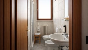 Un baño moderno con ducha, dos inodoros, un lavamanos y una ventana.