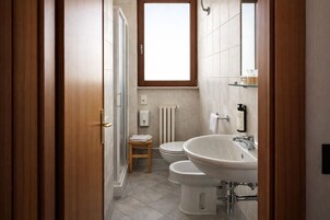 Un baño moderno con ducha, dos inodoros, un lavamanos y una ventana.