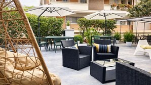 Un patio al aire libre con mobiliario de mimbre, incluyendo sillas y un sofá, y una silla colgante.