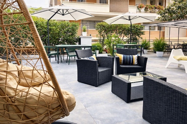 An outdoor patio area with wicker furniture, including chairs and a sofa, and a hanging chair.
