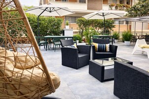 Un patio al aire libre con mobiliario de mimbre, incluyendo sillas y un sofá, y una silla colgante.