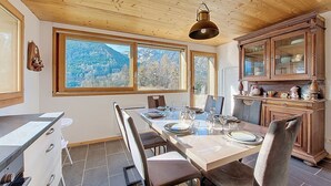 Een eetruimte met een houten tafel voor vier personen, een keuken met houten kasten en uitzicht op bergen door grote ramen.