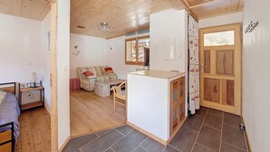 Een gezellige kamer met een houten plafond, een bank, een klein tafeltje en een keukenhoek met een betegelde vloer.