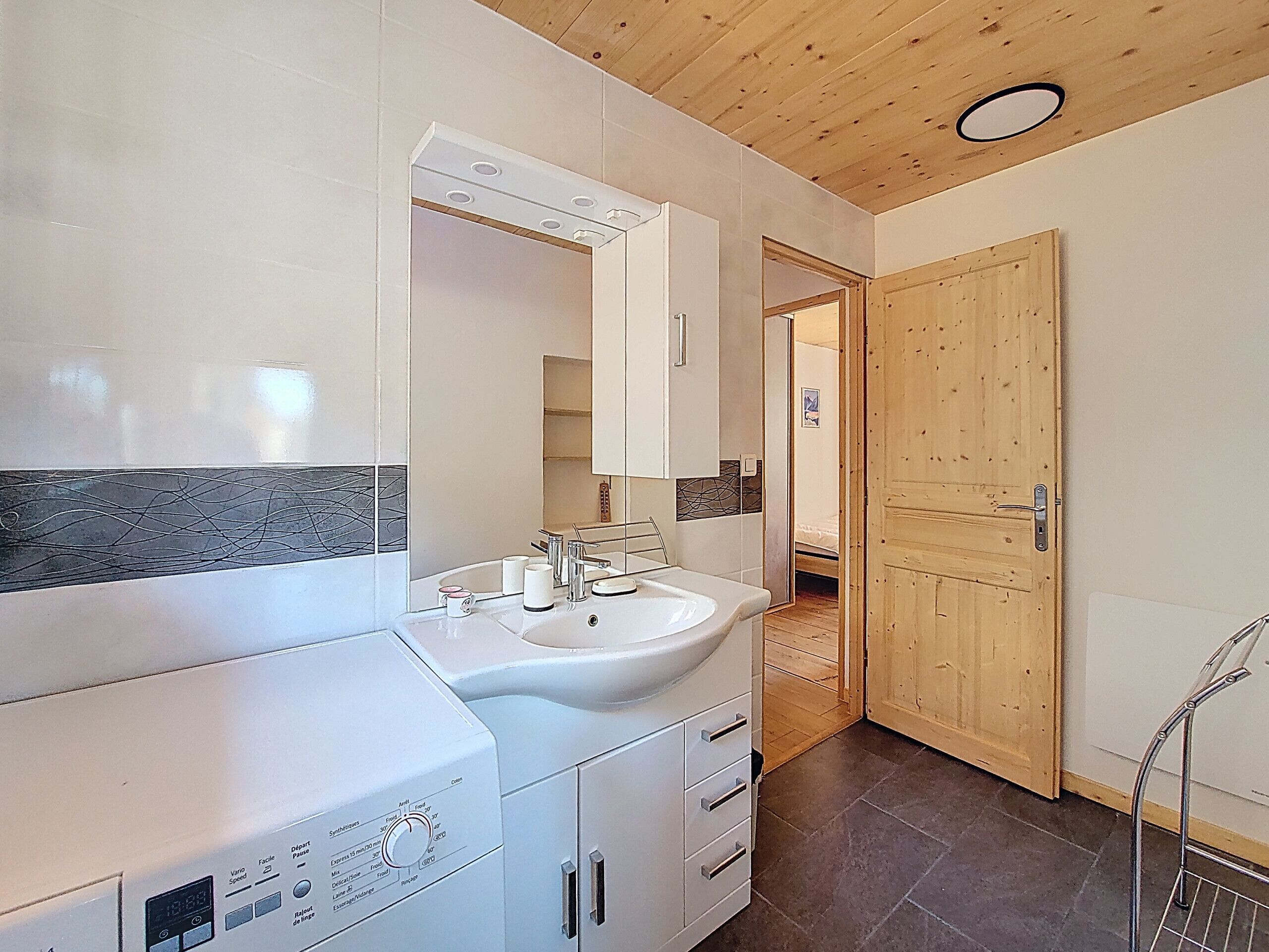 Ein modernes Badezimmer mit einem Doppelwaschbecken, einem Spiegel und einer Holzbalkendecke.