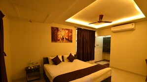A hotel room with a bed, a nightstand, a painting, a ceiling fan, and an air conditioning unit. - SRI VIJAYBALAJI MAHAL  (Tiruvannamalai)