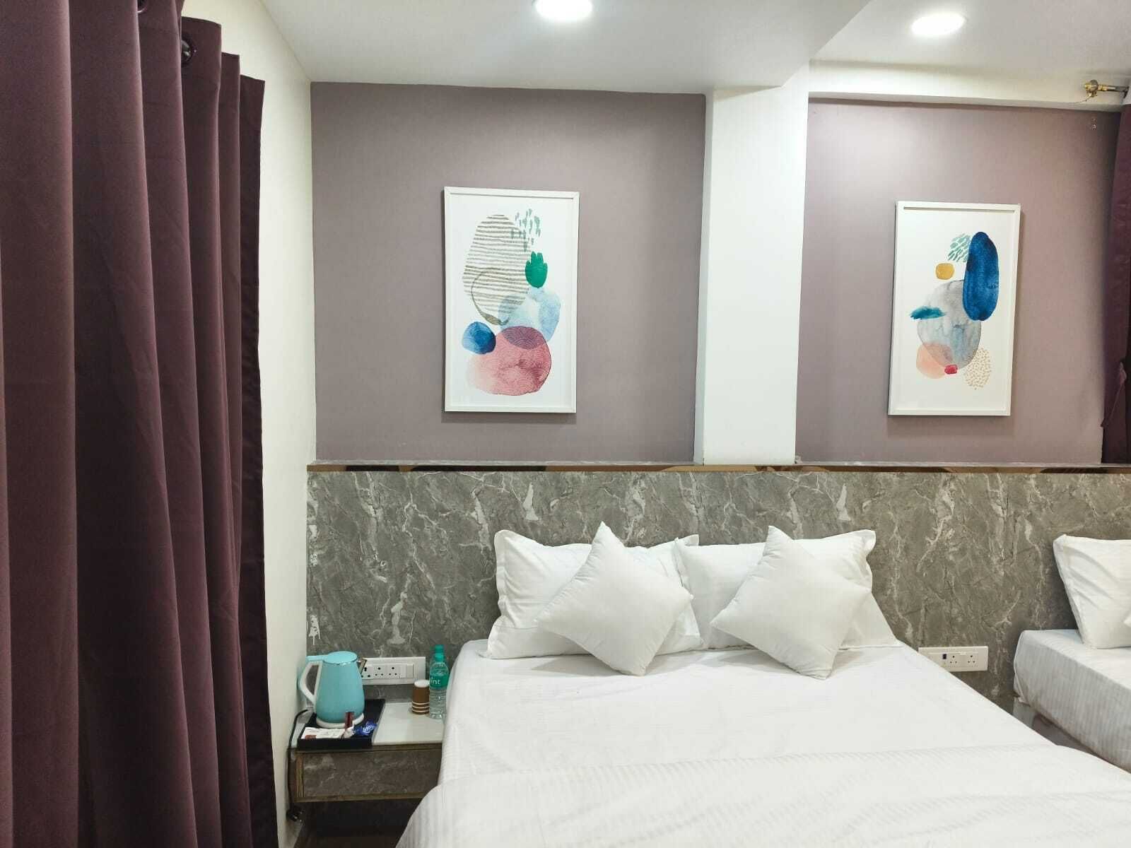 Une chambre d’hôtel avec un lit, une table de chevet, deux œuvres d’art accrochées au mur et un rideau.