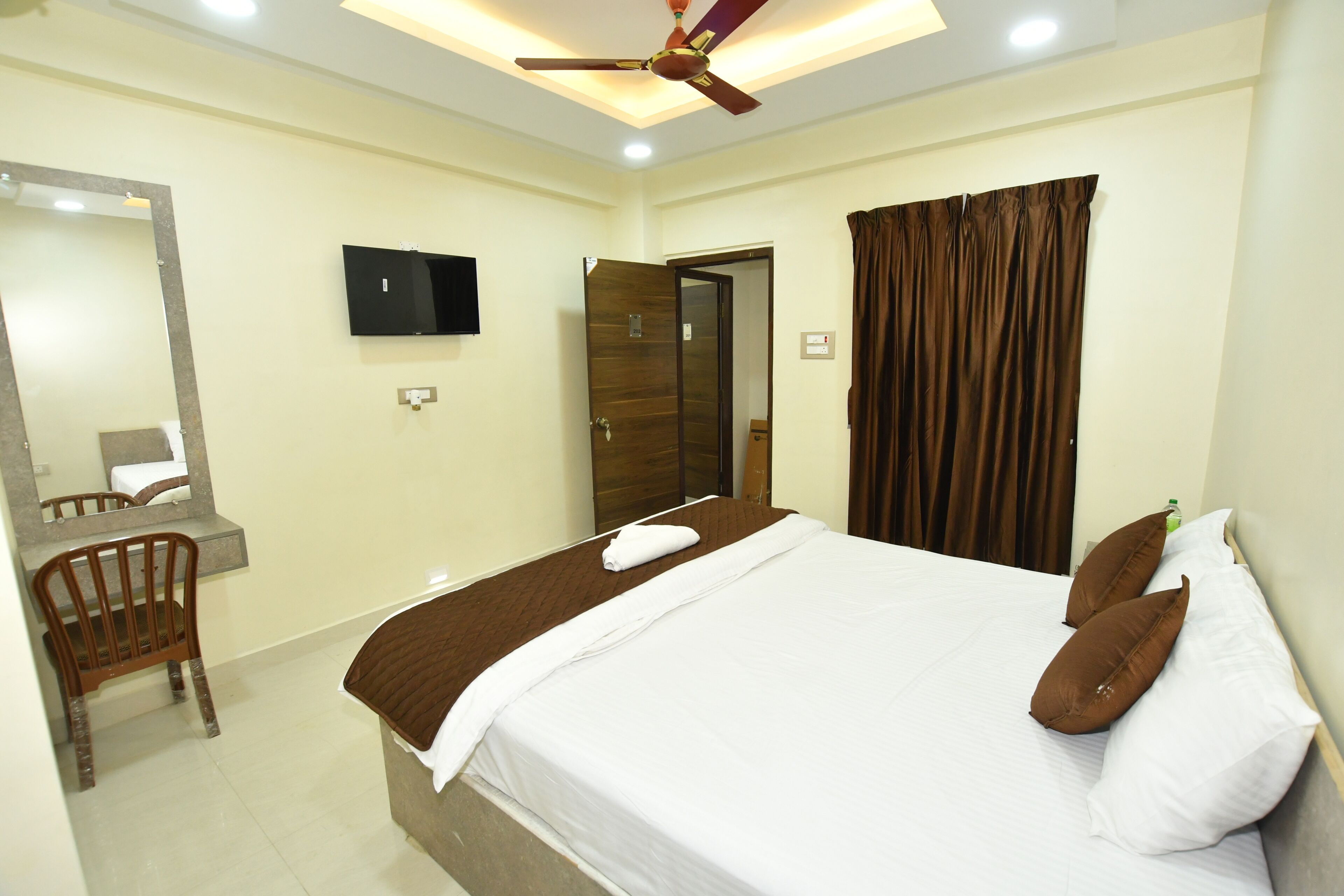 A hotel room with a bed, a desk, a chair, a television, and a ceiling fan.