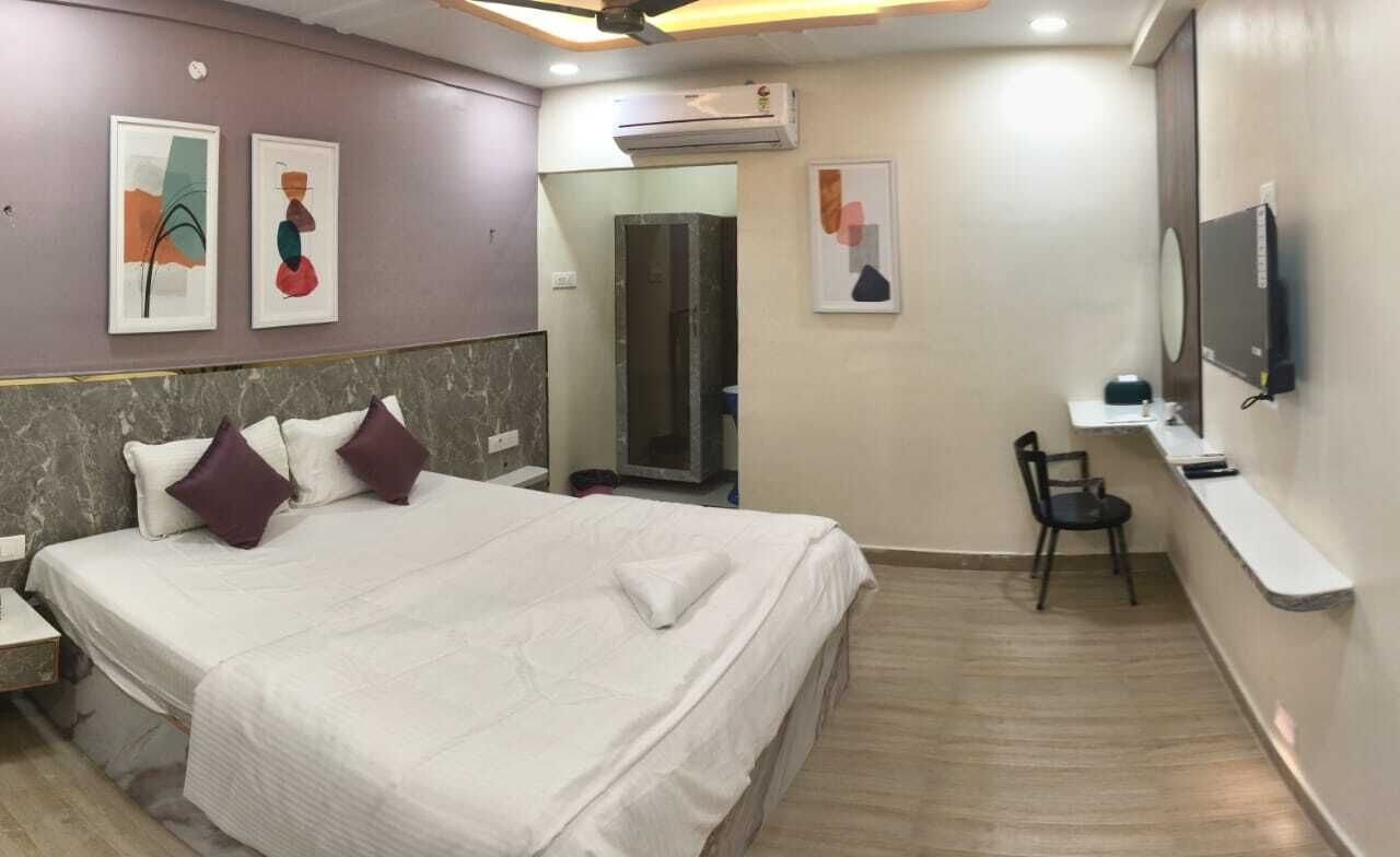 A hotel room with a bed, a desk, a chair, a TV, and artwork on the walls.