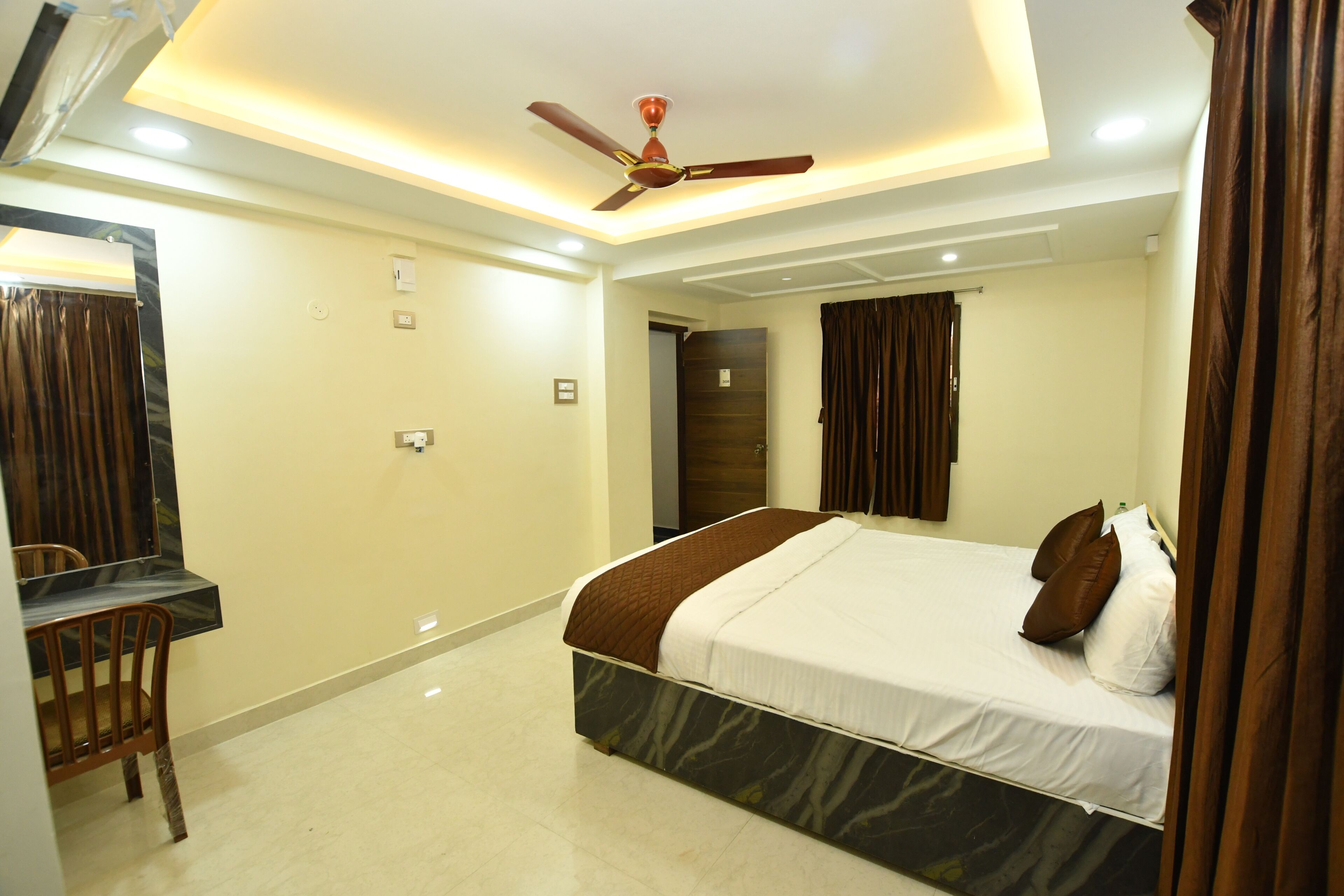 A bedroom with a bed, a desk, a chair, a ceiling fan, and a door.