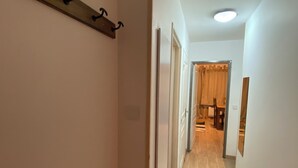A narrow hallway with wooden flooring, a coat rack, and a door leading to a room with a bed and a chair. - La Foux, T3 for 6 people, south-facing, terrace at the foot of the slopes (Allos)