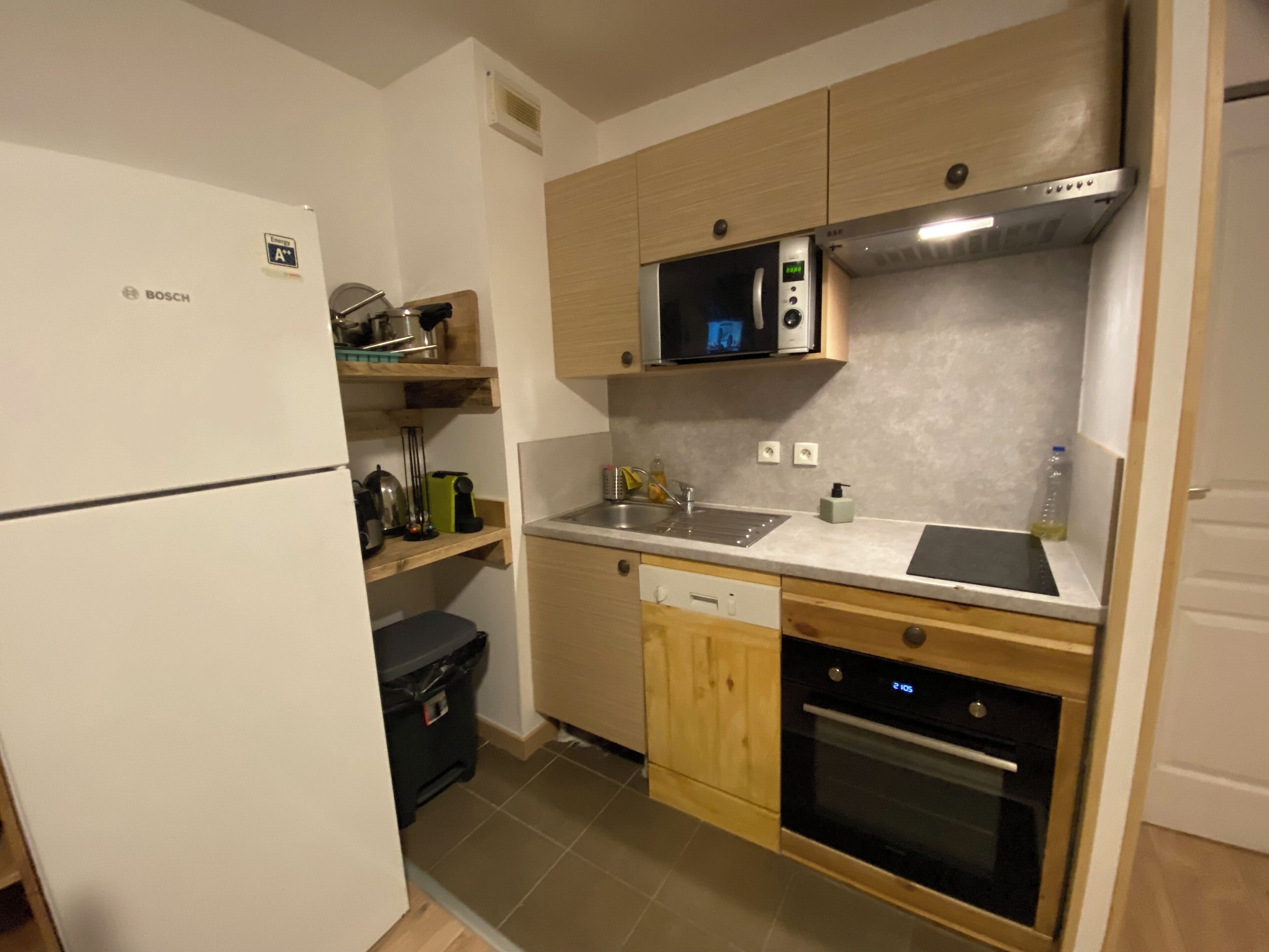 Eine kleine Küche mit einem Kühlschrank von Bosch, einer Mikrowelle, einem Spülbecken und einem Geschirrspüler.