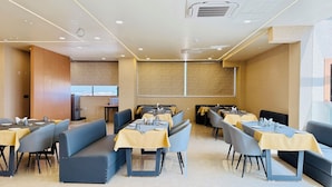 A restaurant with booths and tables, a large window, and a wall-mounted projector screen. - Kreston Heights Hotels Bhopal (Bhopal)