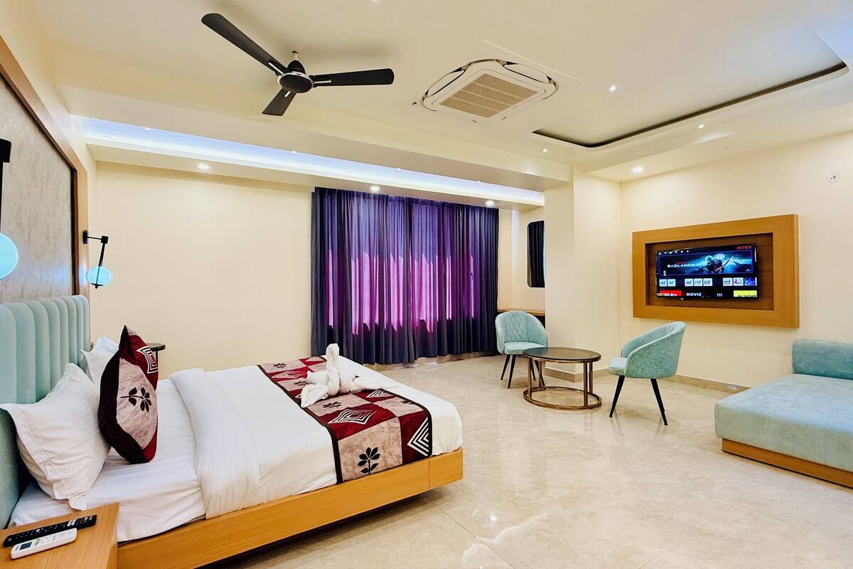 A hotel room with a bed, a ceiling fan, an air conditioner, a TV, and a seating area with chairs and a sofa.