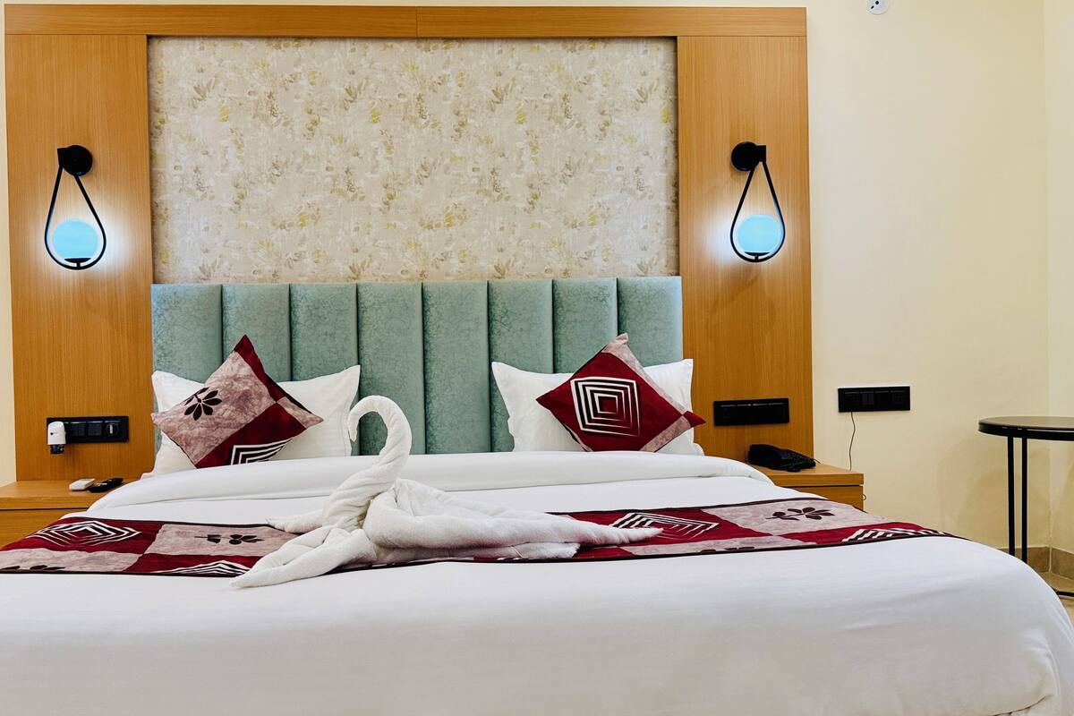 A hotel room with a large bed, a wooden headboard, two wall-mounted lights, and a nightstand with a phone and remote control.