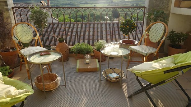 A balcony with two wicker chairs, a small table, potted plants, and a view of the countryside. - Renaissance Room – Provençal Charm and Serenity (Théziers)
