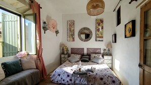 A bedroom with a bed, bedside tables, a window with curtains, a hanging light fixture, and wall decorations. - Renaissance Room – Provençal Charm and Serenity (Théziers)