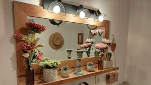 A bathroom vanity with a mirror, shelf, and various toiletries. - Renaissance Room – Provençal Charm and Serenity (Théziers)