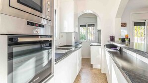 Une cuisine moderne dotée d’appareils électroménagers en acier inoxydable, de meubles blancs et offrant une vue sur l’extérieur à travers une porte en arc de cercle.