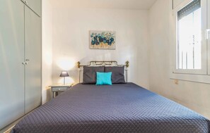 Ein Schlafzimmer mit Bett, Nachttisch, Lampe, Wandbild und Fenster.