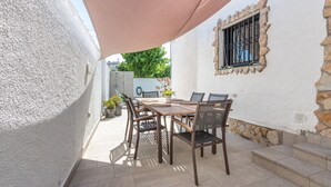 Une terrasse avec une table et des chaises, un pot de fleurs et un mur en pierre.
