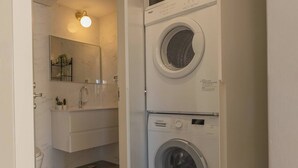 A compact bathroom with a sink, mirror, and two stacked washing machines. - 1 BR Apartment in Ha-Neviim (w/ safe room) (Jerusalem)