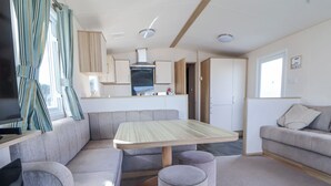A modern living room with a sofa, ottoman, and a dining table. - The Beachside Hideout - St Michaels Caravan Park (Abergele)
