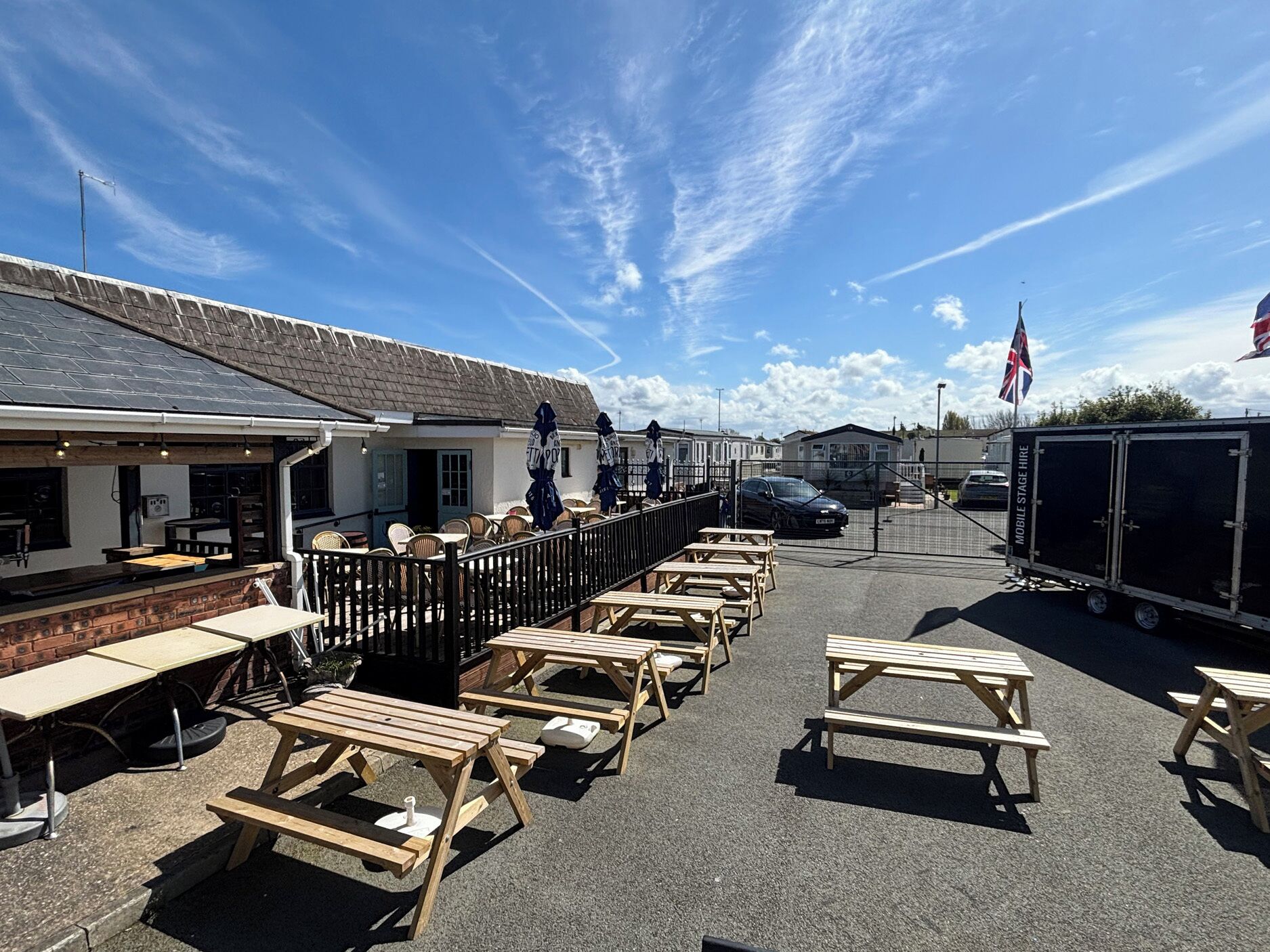 A caravan park with wooden picnic tables, a covered seating area, and a mobile stage hire trailer.