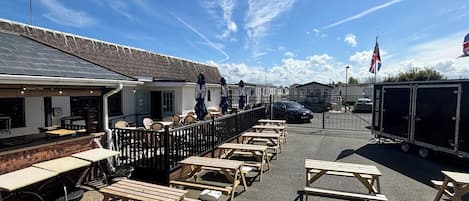 A caravan park with wooden picnic tables, a covered seating area, and a mobile stage hire trailer.