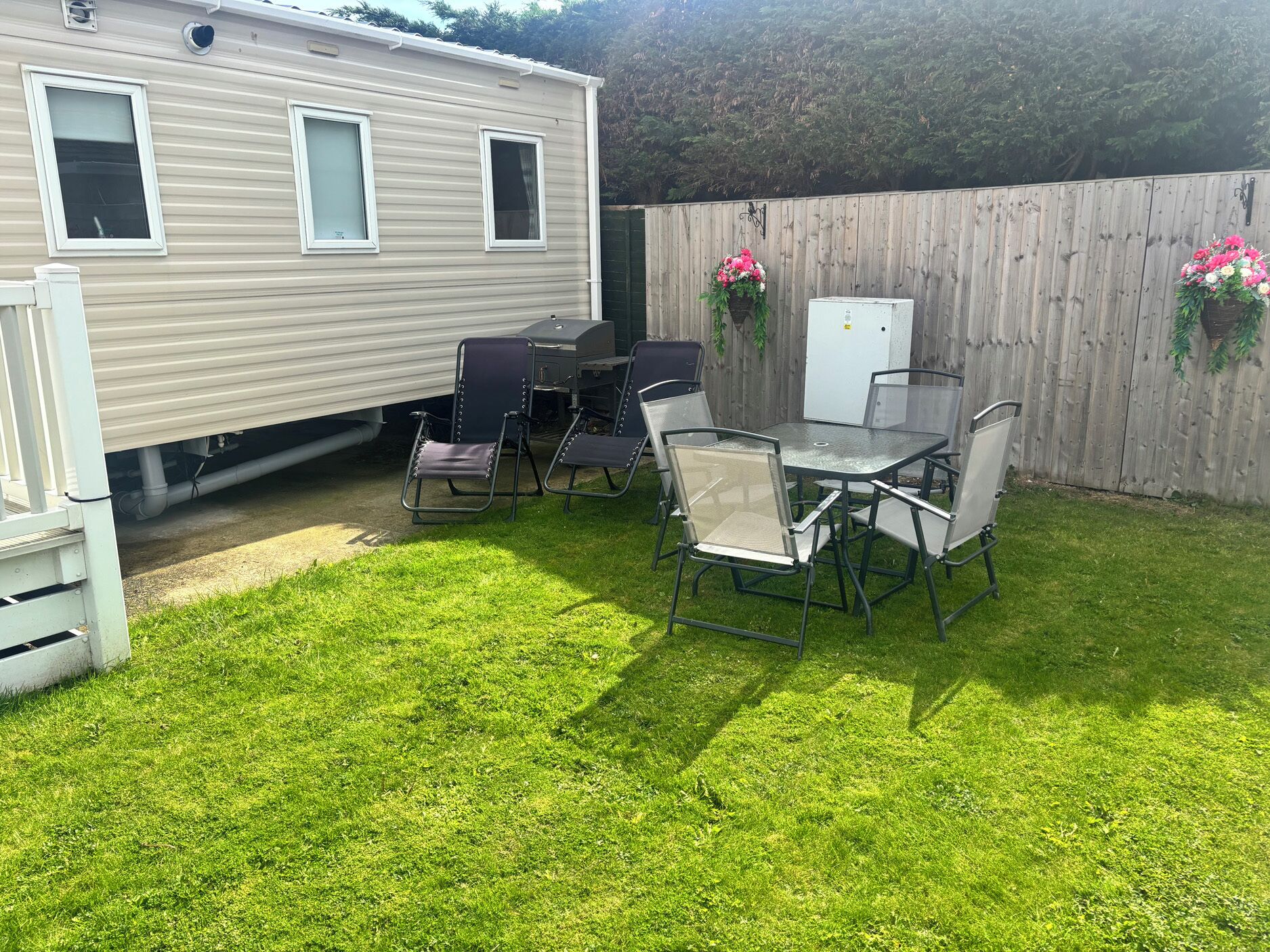 A mobile home with a patio area featuring a table and chairs, a grill, and a small refrigerator.