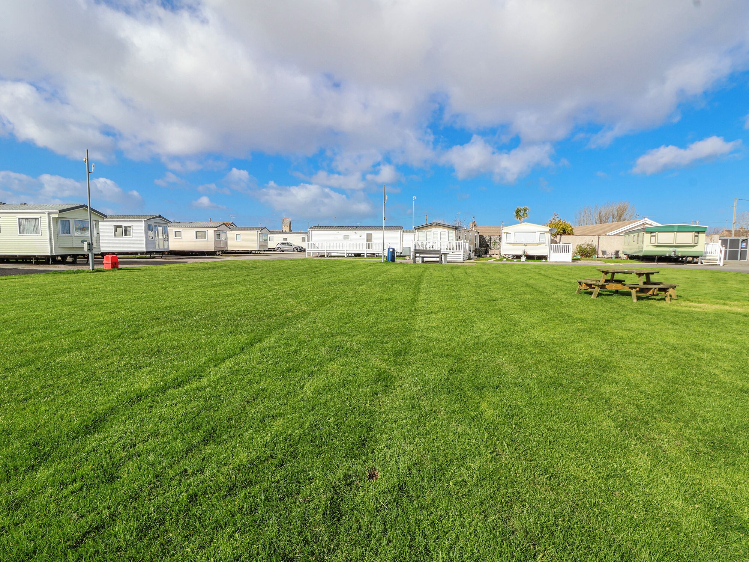A grassy field with mobile homes, a picnic table, and a clear sky.