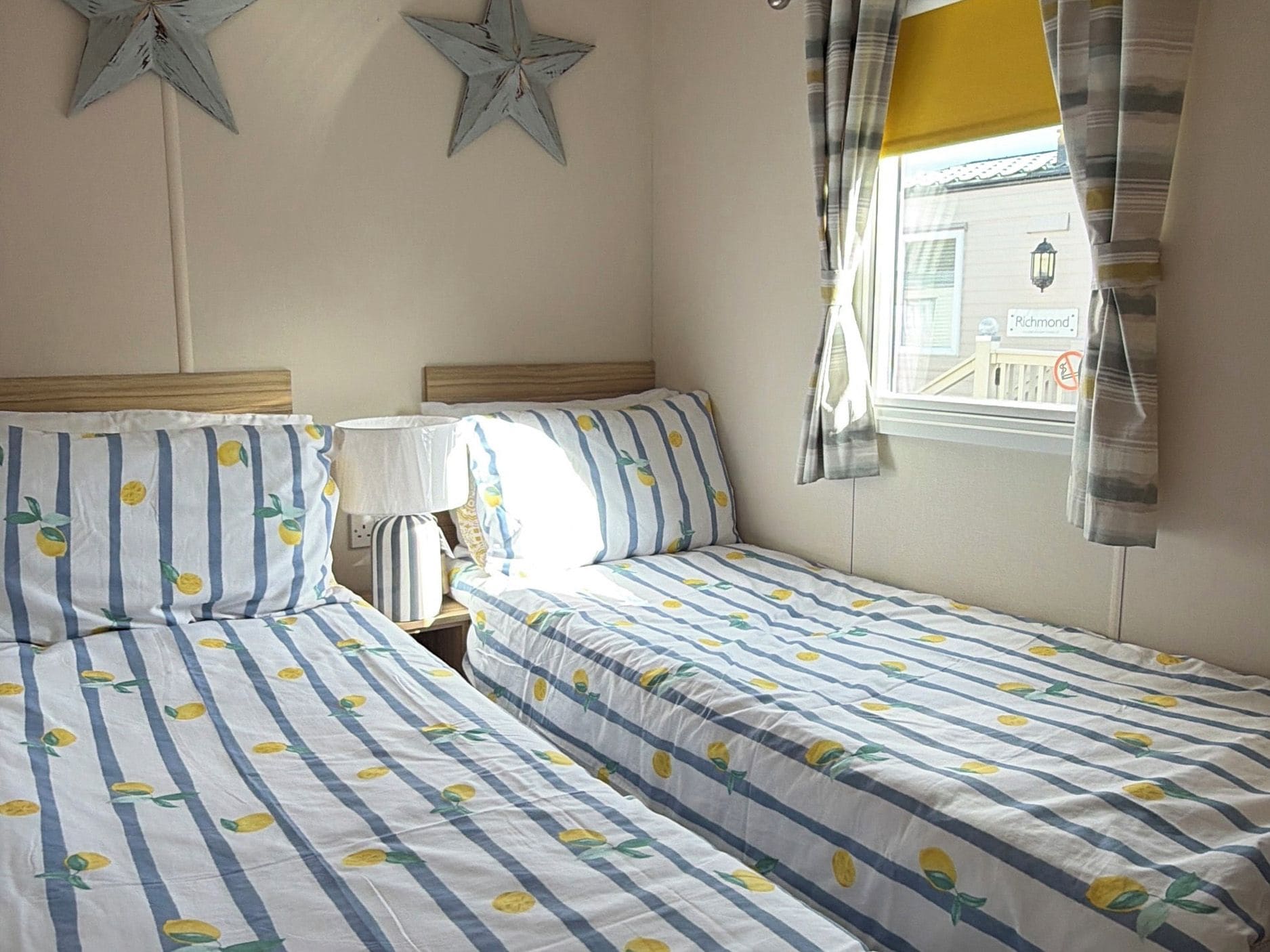 Un dormitorio con dos camas, ropa de cama a rayas, una mesita de noche, una lámpara y una ventana con cortinas.