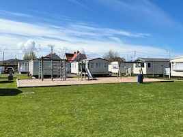 Zona verde con un parque infantil, viviendas móviles y cielo despejado.