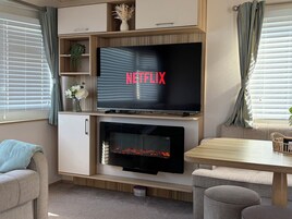 A modern living room with a flat-screen TV mounted above a fireplace, a sofa, and a dining table.