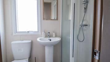 Un baño con inodoro, lavamanos y ducha con mampara de vidrio.