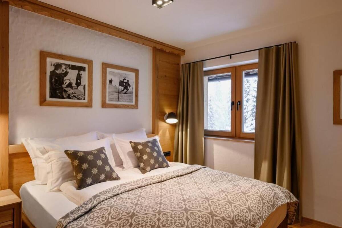 A bedroom with a bed, two framed pictures on the wall, a bedside lamp, and a window with curtains.