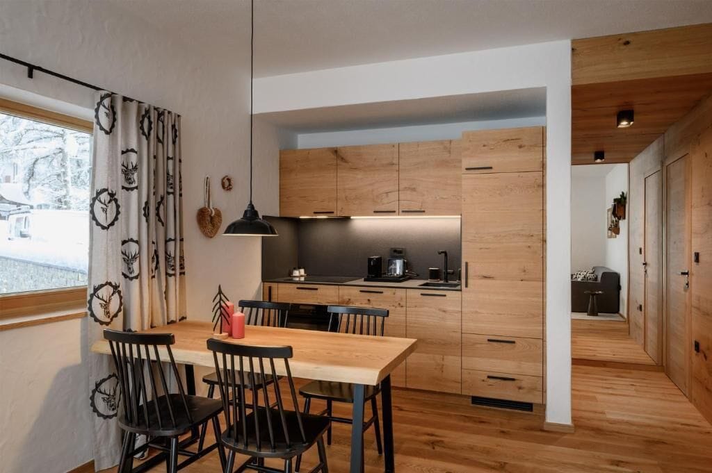 A modern kitchen with wooden cabinets, a dining table with chairs, and a pendant light.