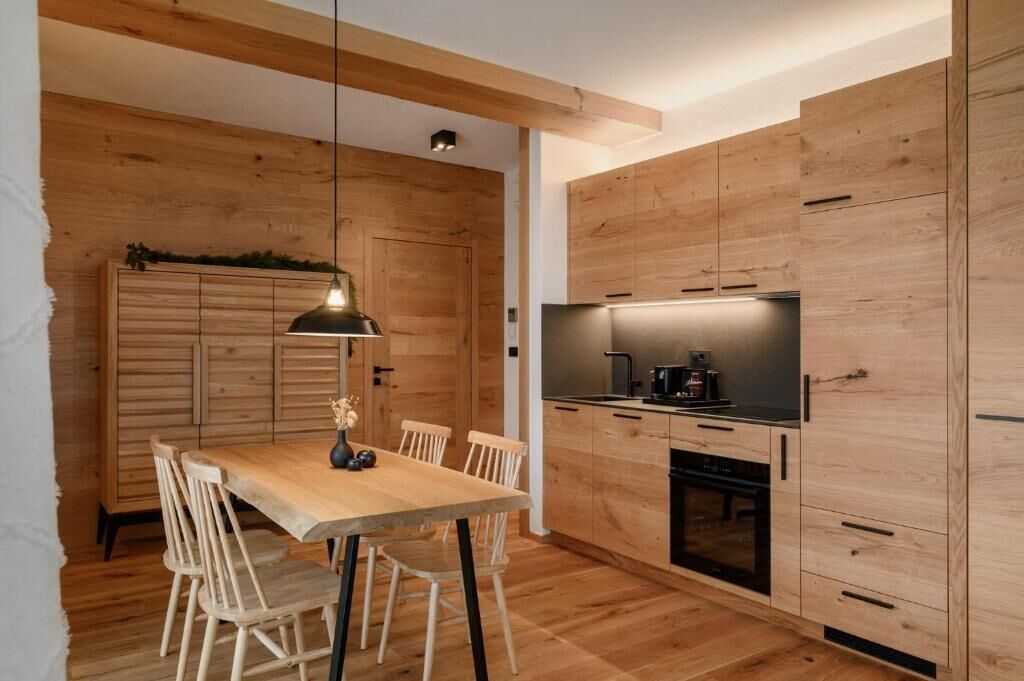 A modern kitchen with wooden cabinetry, a dining table with chairs, and a pendant light.