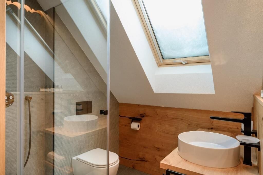 Une salle de bain moderne dotée d’un puits de lumière, d’une cabine de douche en verre, de toilettes et d’un meuble-lavabo en bois avec un évier.