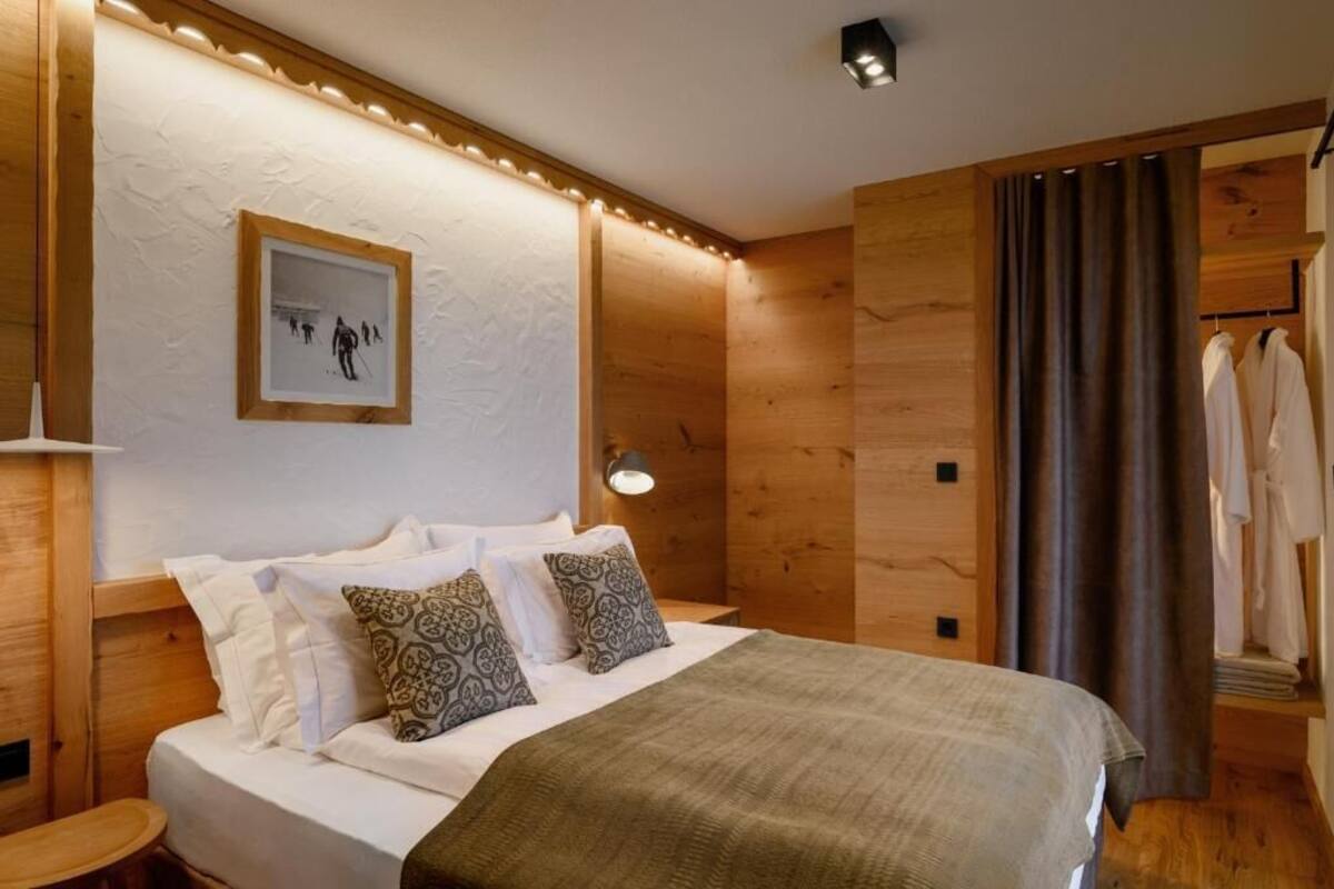 A hotel room with a wooden headboard, a bed with patterned pillows, a framed artwork on the wall, and a window with curtains.