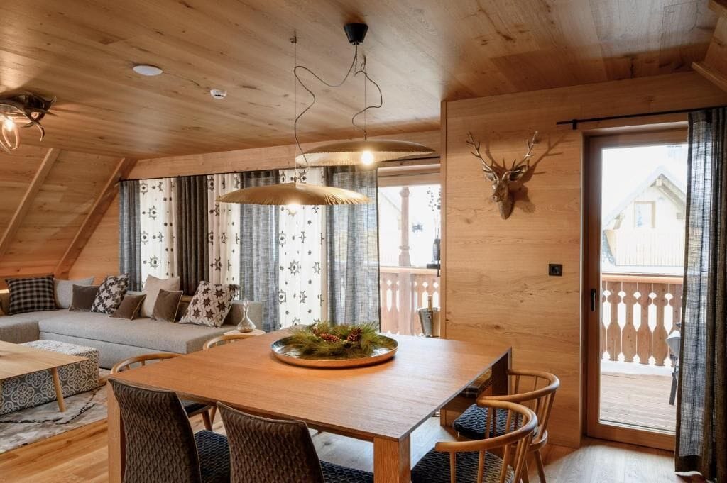 Un intérieur chaleureux en bois, avec une table à manger, des chaises, un canapé et une grande fenêtre agrémentée de rideaux.