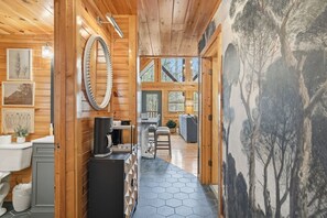 A wooden cabin interior with a kitchen area, a dining space, and a large window overlooking trees. - Pine & Dandy | Arts & Crafts District Cabin w/ Hot Tub & Game Features (Gatlinburg)