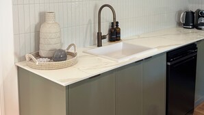 Eine Küche mit weiß gefliestem Spritzschutz, einer Uhr in Holzrahmen, einem Spülbecken und einer Kaffeemaschine.