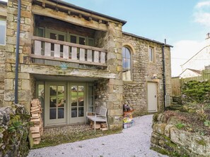 Un edificio in pietra con un balcone, una recinzione in legno e un vialetto sterrato.