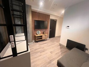 Ein modernes Wohnzimmer mit Flachbildfernseher, einer Holzwand und einem grauen Sofa.