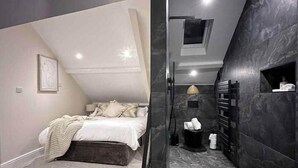 Un dormitorio moderno con techo inclinado, una cama, un pequeño rincón de descanso y un baño de tonos oscuros con un perchero para toallas.